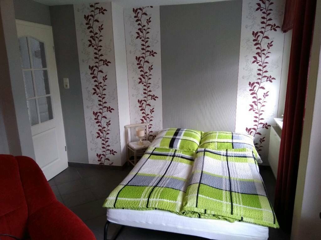 Una habitació amb un llit, una cadira vermella i una porta.