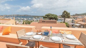 Eine Terrasse mit Esstisch, mit Blick auf eine Marina mit Booten und einem Baum.