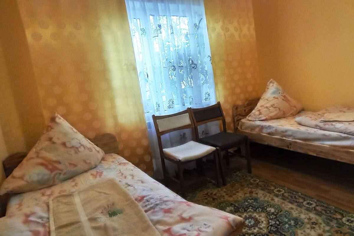 Ein kleines Zimmer mit zwei Einzelbetten, einem Sessel und einem Fenster mit Vorhängen.