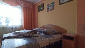 Un dormitorio con cama, almohadas, una mesita de noche y una ventana con cortinas.