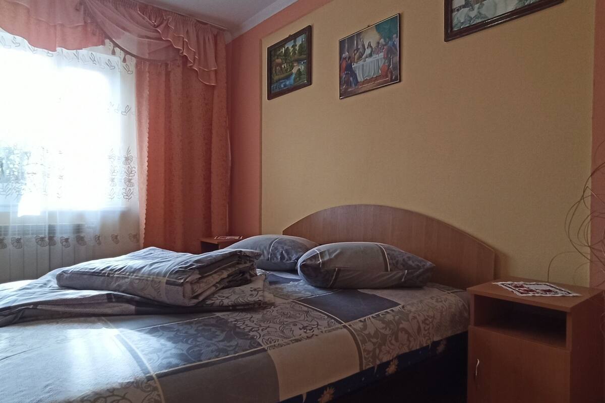 Ein Schlafzimmer mit Bett, Kissen, einem Nachttisch und einem Fenster mit Vorhängen.