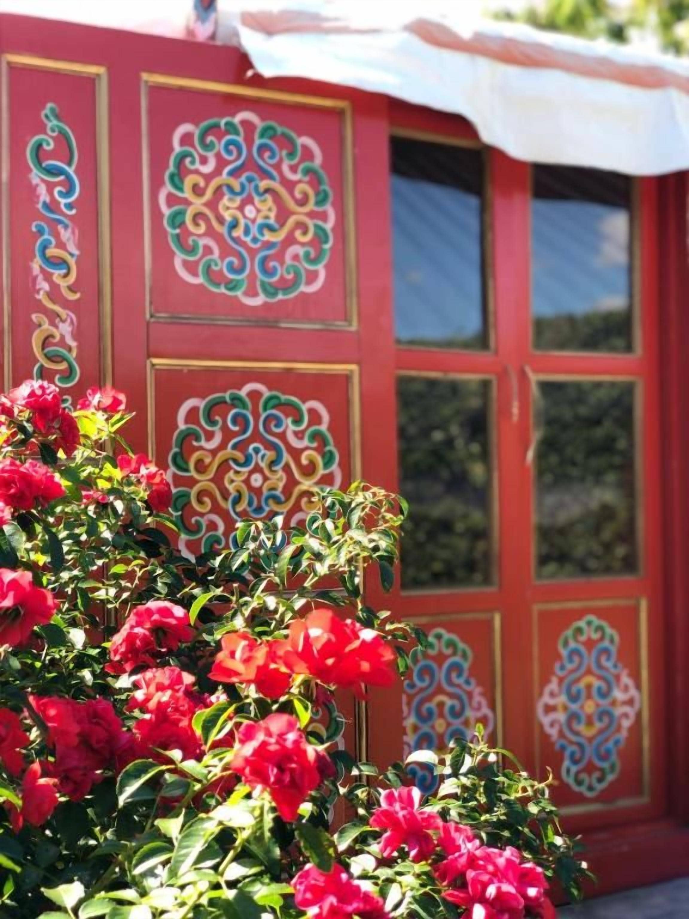 Um edifício vermelho com desenhos decorativos e um arbusto de flores em primeiro plano.