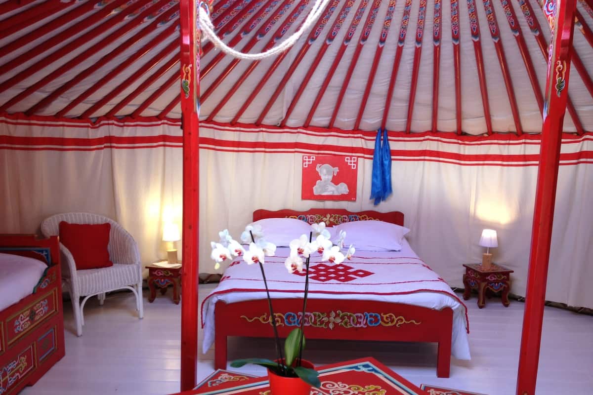 A traditional yurt bedroom with a bed, a chair, and a small table with a plant.