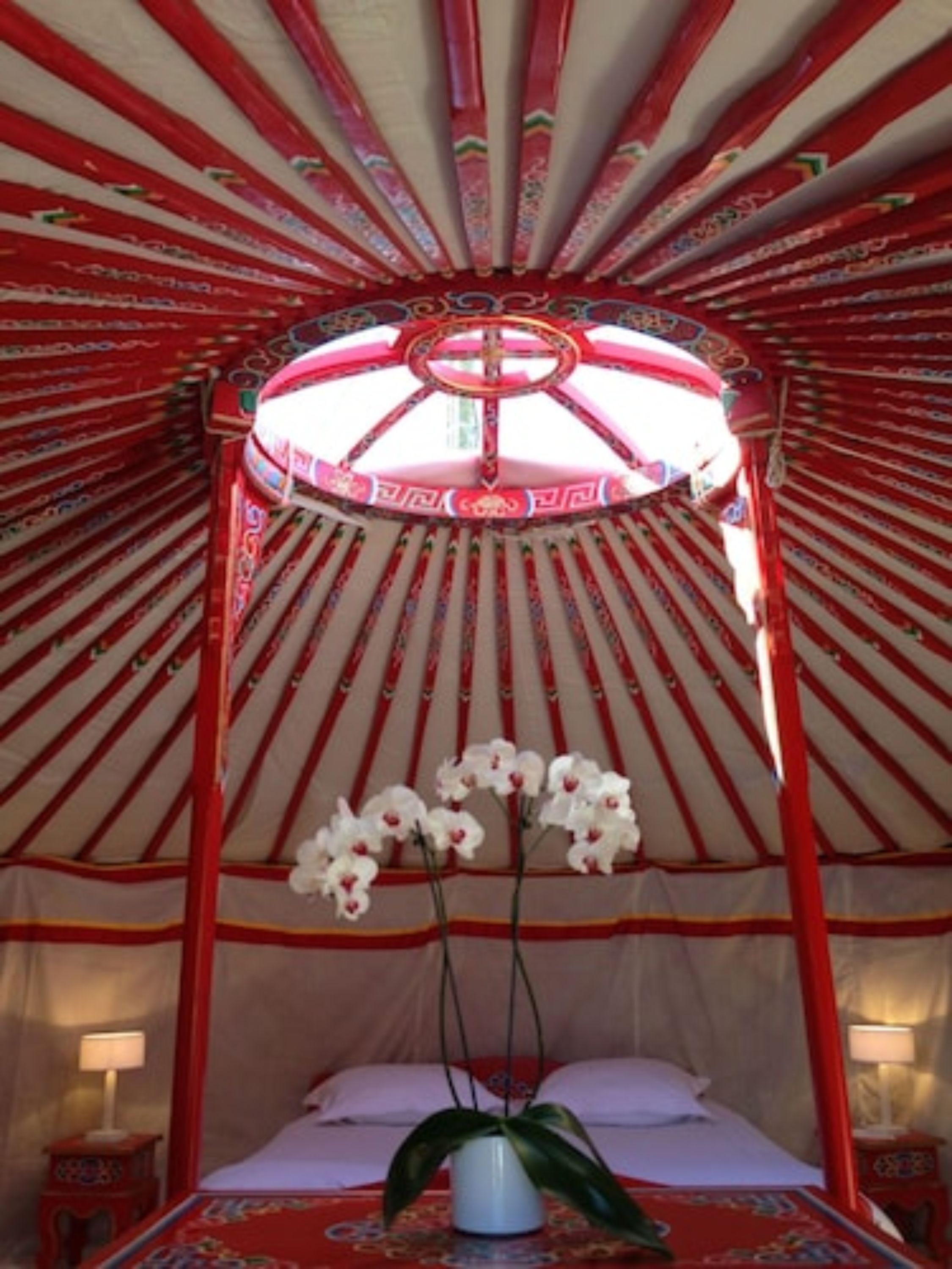 A traditional yurt with a bed, a decorative canopy, and a vase with flowers.