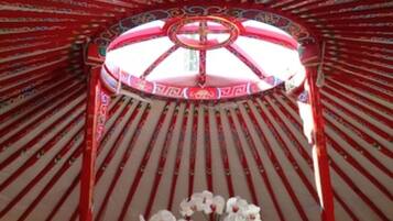 A traditional yurt with a bed, a decorative canopy, and a vase with flowers.