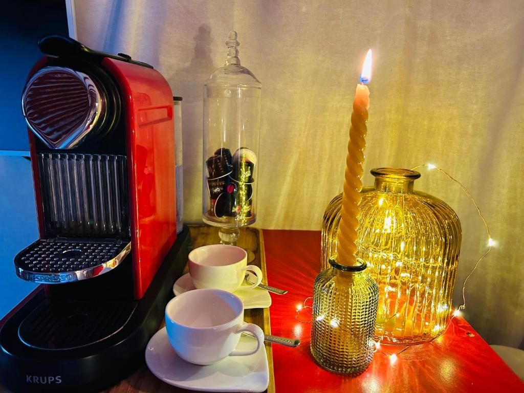 Una cafetera, dos tazas, una vela y una botella decorativa sobre una mesa.