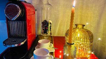 Una cafetera, dos tazas, una vela y una botella decorativa sobre una mesa.