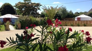 A garden with red flowers, a white tent, and a wooden fence. - Yourte au Paradis (Souvigné)