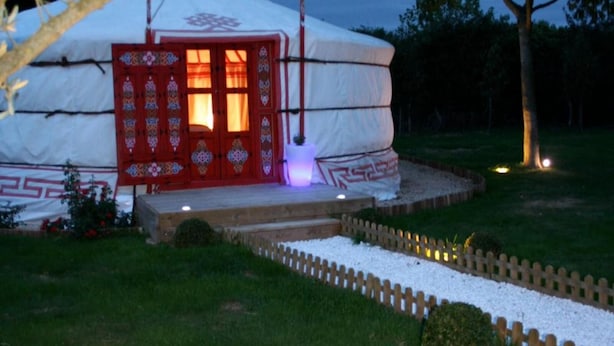 A yurt with a red door and a small porch area, surrounded by a garden with lavender plants and a wooden fence. - Yourte au Paradis (Souvigné)