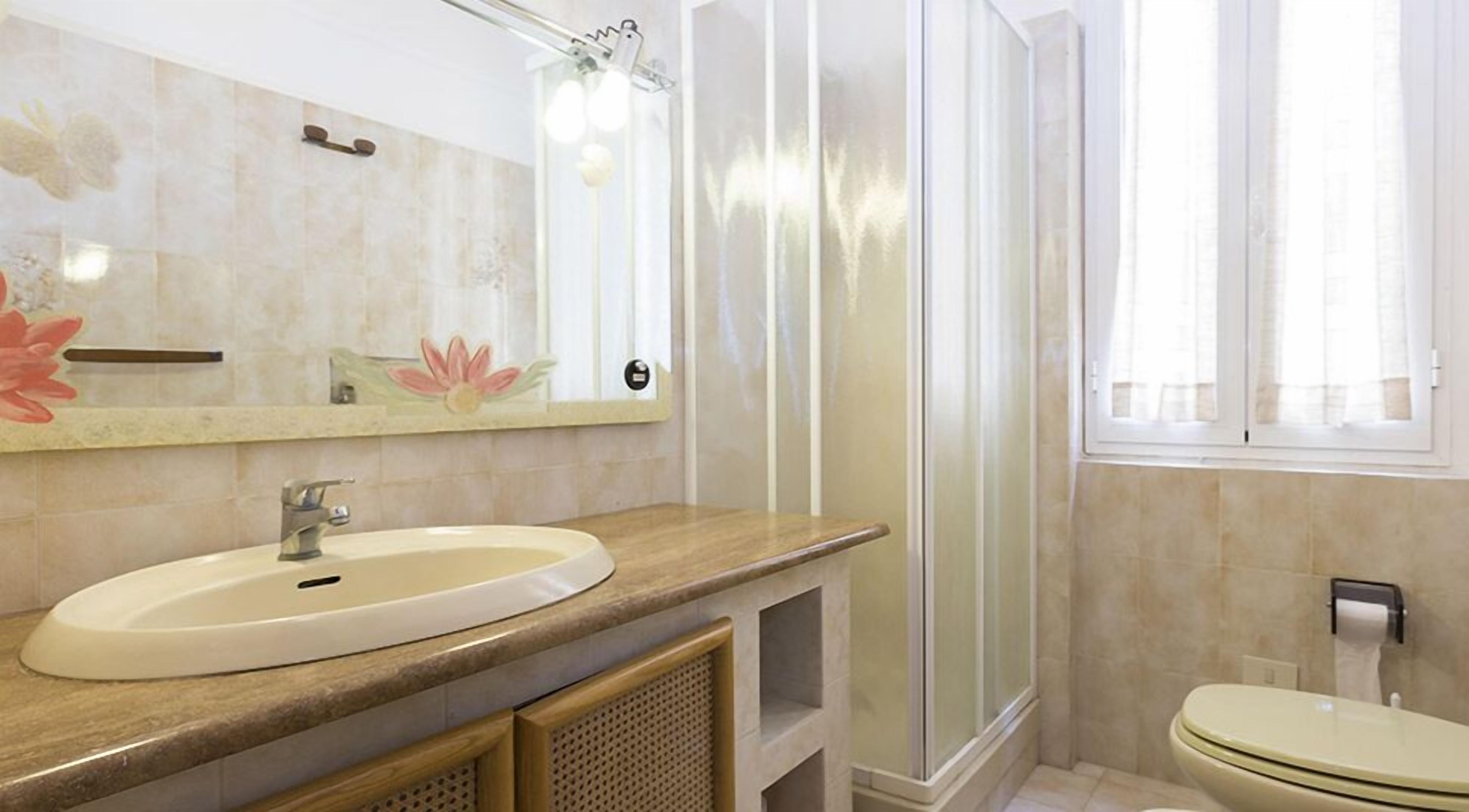 A bathroom with a sink, mirror, shower, toilet, and a window.