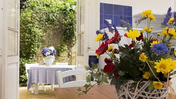 An outdoor dining area with a table and chairs, a wicker basket with flowers, and a wall with blue tiles. - Belmare (Porto Azzurro)