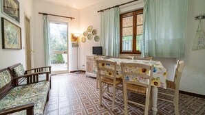 Uma área de refeições com uma mesa posta para quatro pessoas, um sofá e uma televisão sobre um móvel.
