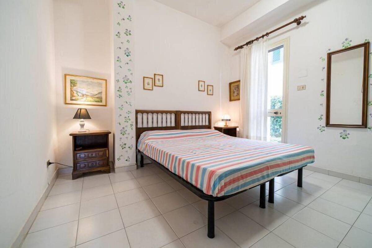 Une chambre à coucher comprenant un lit, deux tables de chevet, une commode, une fenêtre avec des rideaux et des tableaux accrochés au mur.