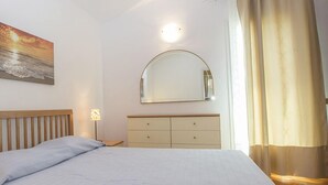 Quarto com cama, mesa de cabeceira, cômoda, espelho e um quadro na parede.