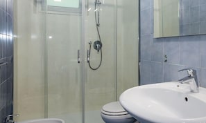 Uma casa de banho moderna com chuveiro de cabine de vidro, lavatório branco e sanita.
