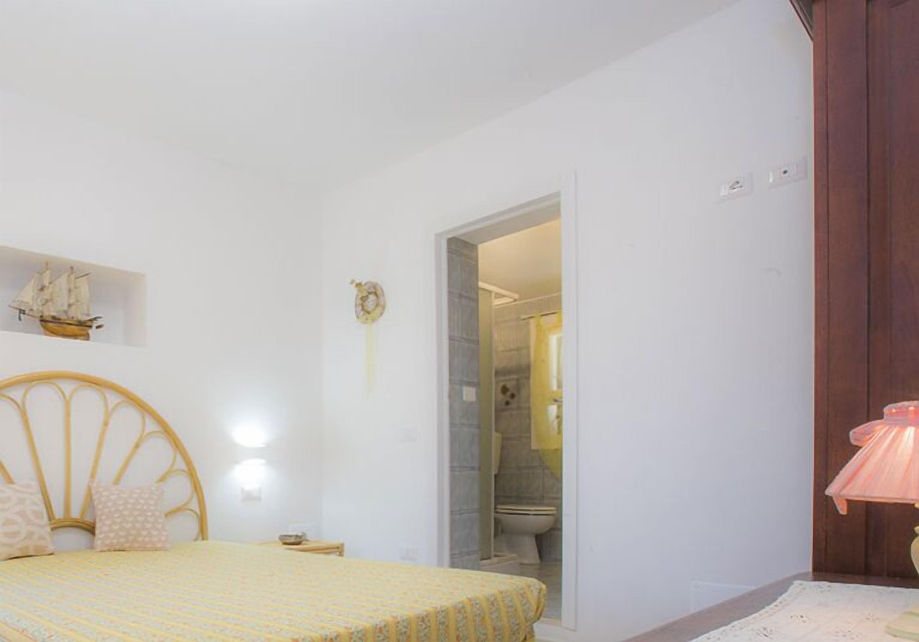 Un dormitorio con cama, una mesita de noche, una lámpara y una estantería con un modelo de barco.
