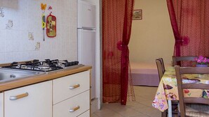 Una cucina con lavello, fornello e frigorifero. Si nota un tavolo da pranzo con una sedia e una tenda rossa sullo sfondo.