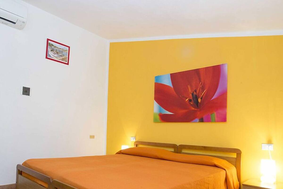 A hotel room with a bed, a yellow wall, and a painting of a flower.