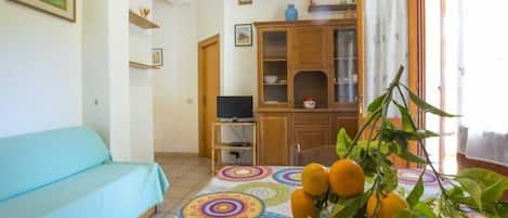 A living room with a sofa, a television, a cabinet, and a table with a patterned tablecloth and oranges.
