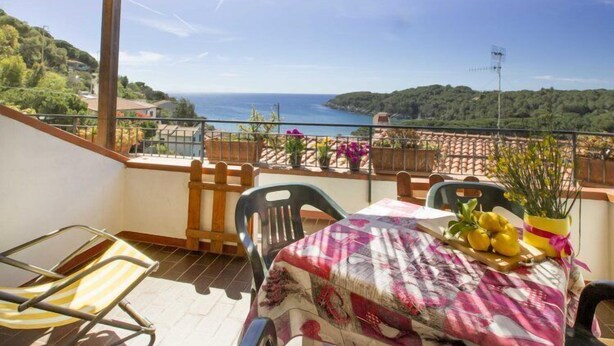 Un balcone con un tavolo apparecchiato per due, sedie e vista sul mare.
