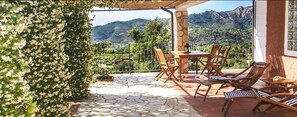 An outdoor patio with stone flooring, wooden furniture, and a view of mountains.