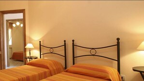 Een kamer met twee enkele bedden, een houten deur, een tafeltje met een lamp en een spiegel.