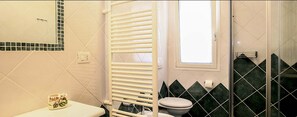 A bathroom with a toilet, a towel rack, a window, and a shower area.