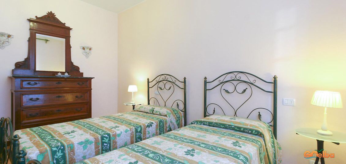A bedroom with two single beds, a wooden dresser, a mirror, and two wall-mounted lamps.