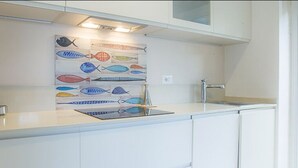 Een moderne keuken met witte kasten, een roestvrijstalen spoelbak en een spatwand met kleurrijke tekeningen van vissen.