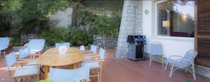 An outdoor patio with a round wooden table and chairs, a stone wall, and a grill.
