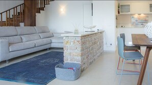 Een moderne woonkamer met een bank, een eettafel met stoelen, een accentmuur van steen, en een keuken op de achtergrond.