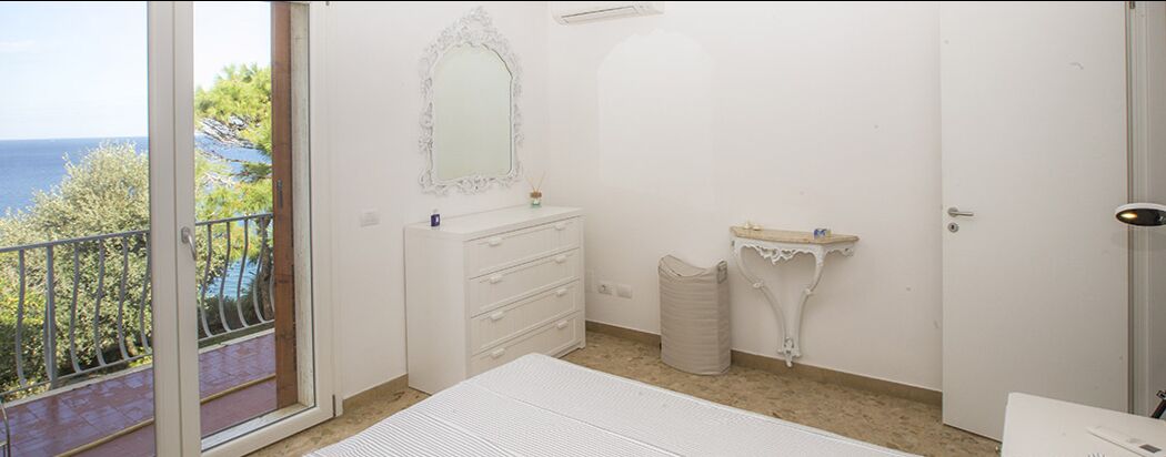 A bedroom with a balcony, a white dresser, a vanity with a mirror, and a door.