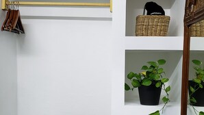 Un baño con pared blanca, repisa de madera con plantas en macetas, una cesta de mimbre y un perchero para toallas.