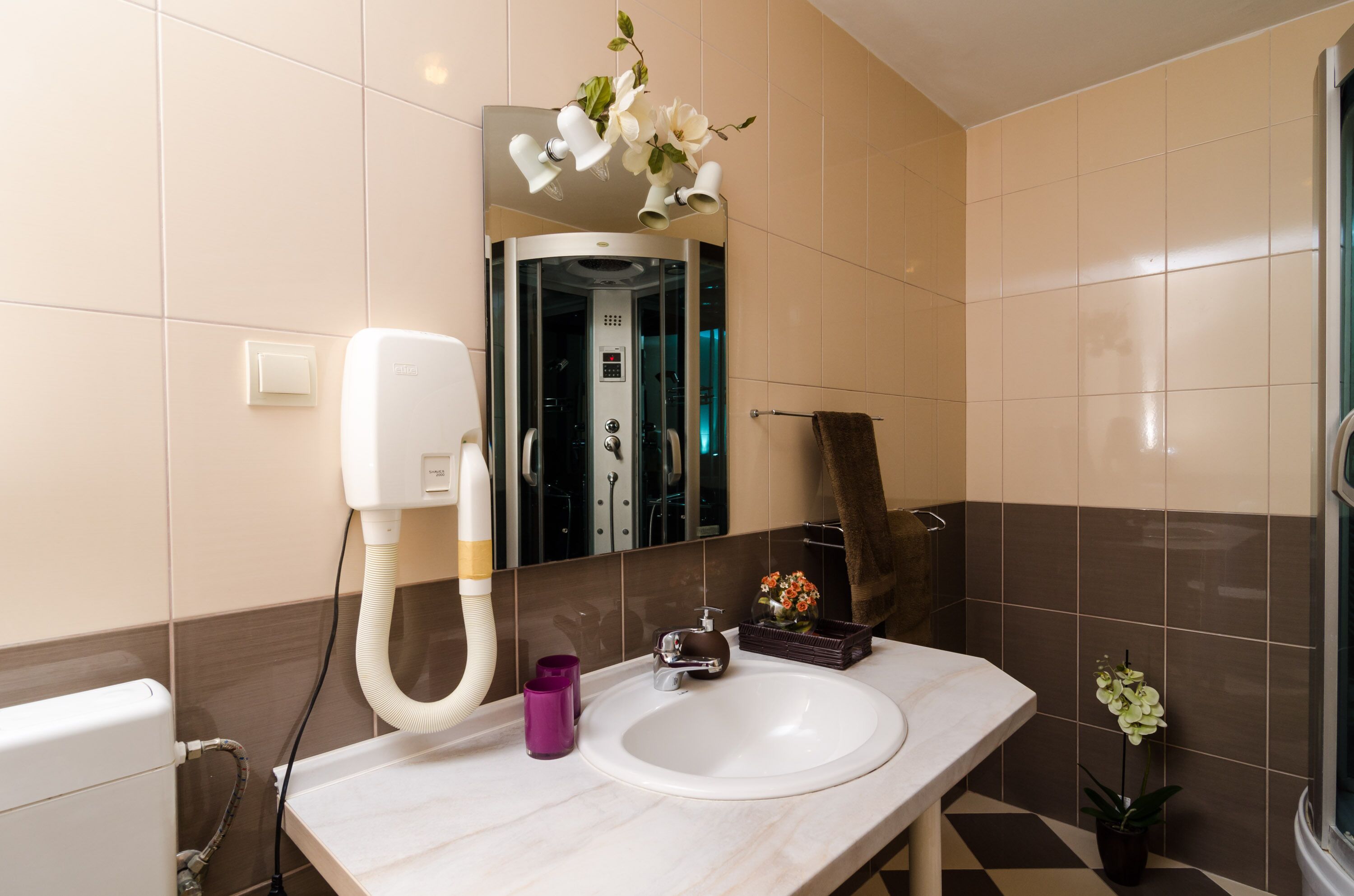 Ein Badezimmer mit weißem Waschbecken, einem Spiegel, einem Handtuchhalter, einer Dusche und einer Toilette.
