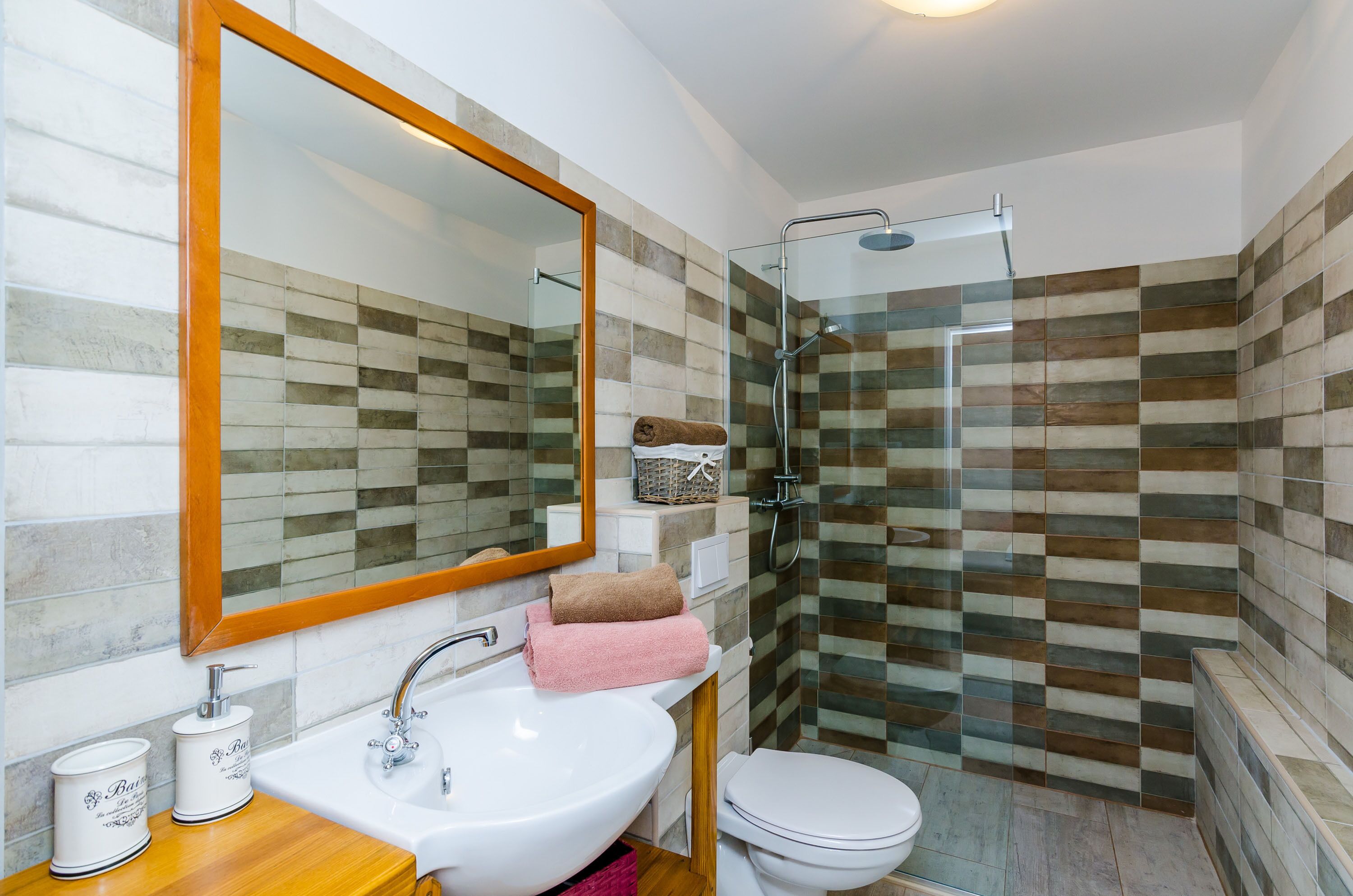 Un bagno con un lavandino bianco, uno specchio, una doccia con porta in vetro e un water.