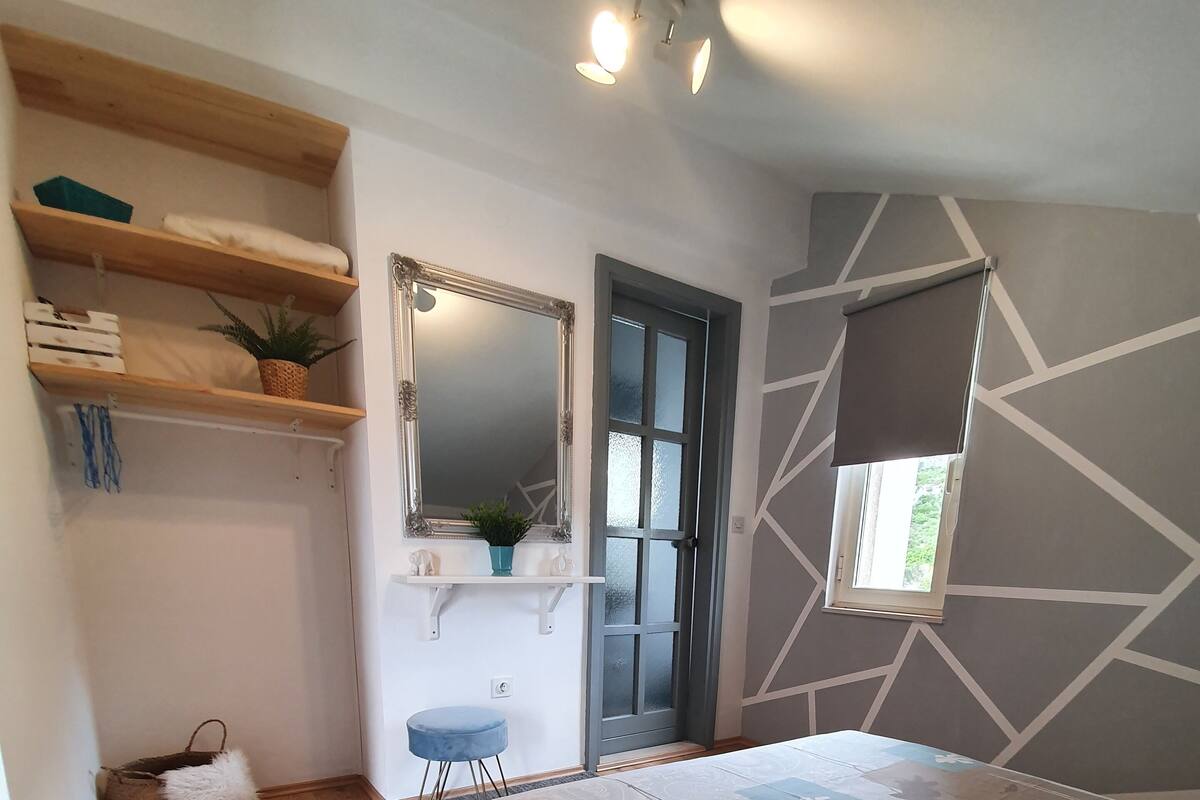 Ein Schlafzimmer mit Bett, Holzboden, Spiegel, Fenster und eingebauten Regalen.