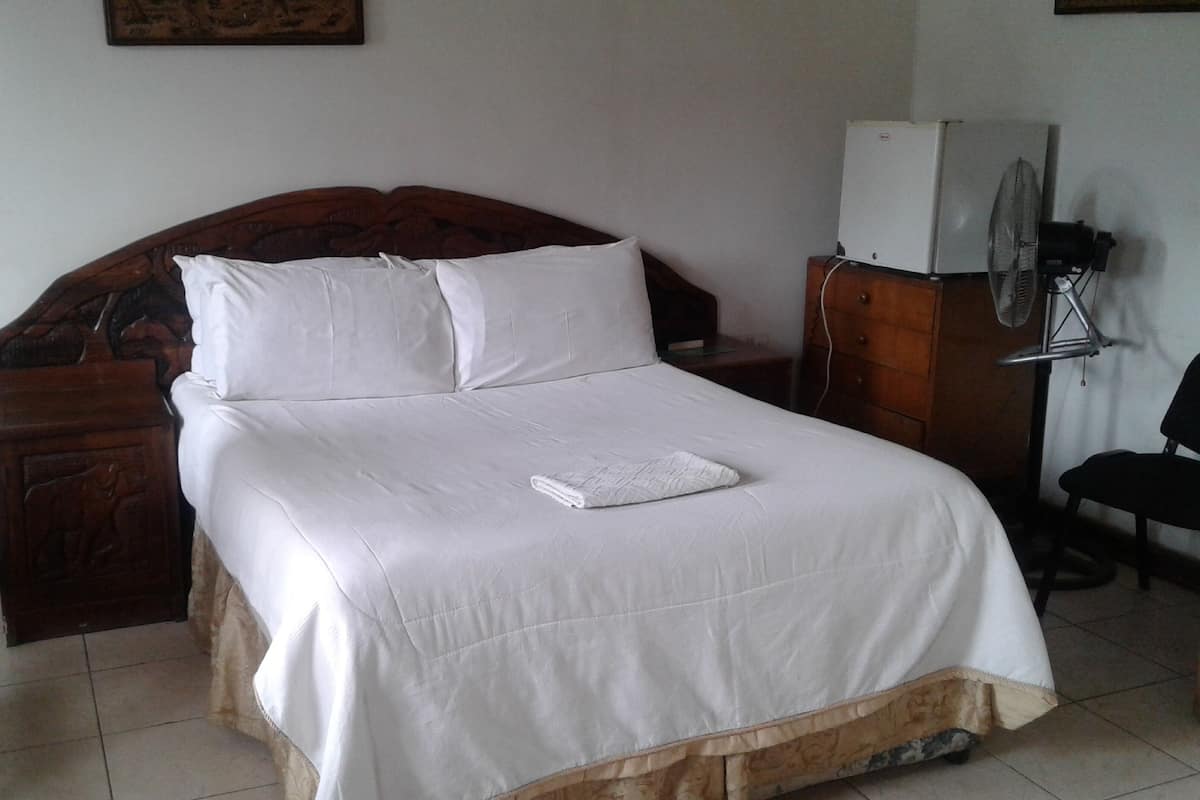 A neatly made bed with white linens, a wooden headboard, and a bedside table with a fan.