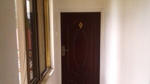 Un couloir étroit avec une porte sombre et une fenêtre sur le côté gauche.