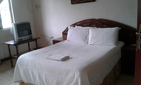 A bedroom with a bed, a television on a small table, and a wall socket. - Providence Teez Lodge (Kitwe)