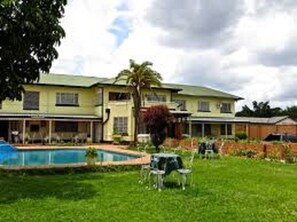 A two-story building with a swimming pool, outdoor seating, and a well-maintained lawn. - Providence Teez Lodge (Kitwe)
