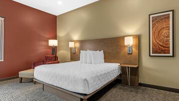 Quarto de hotel com cama, luminárias de cabeceira, uma cadeira e um grande quadro abstrato na parede.