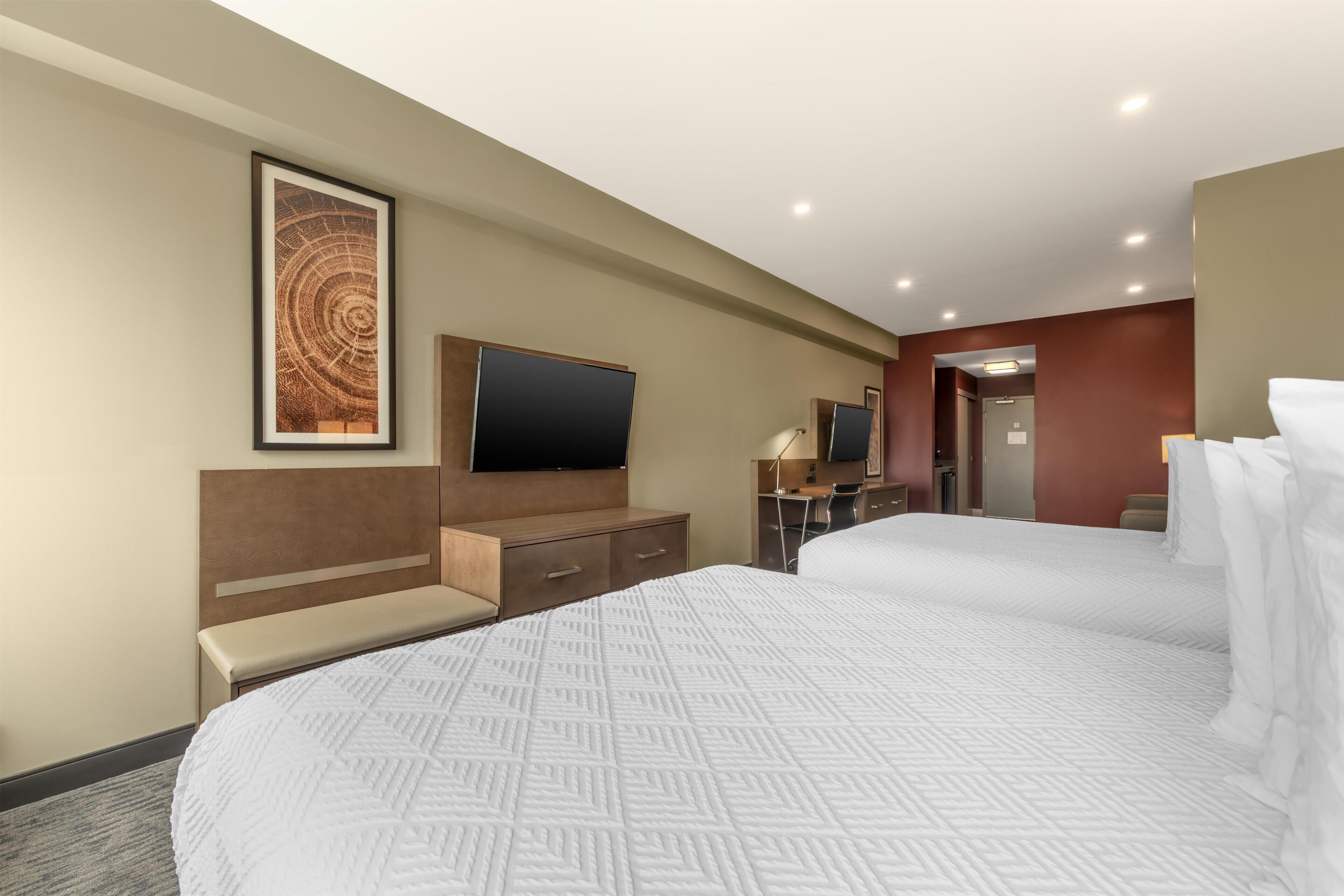 A hotel room with two beds, a desk, a television, and a framed artwork on the wall.