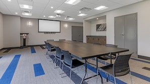 A conference room with a long table, chairs, a projector screen, and a podium. - Best Western Plus Dauphin (Dauphin)