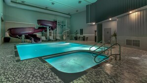 An indoor swimming pool with a slide, a staircase, and a seating area with tables and chairs. - Best Western Plus Dauphin (Dauphin)