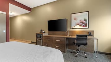 Quarto de hotel com uma cama, uma escrivaninha com cadeira, televisão de tela plana, micro-ondas e um quadro na parede.