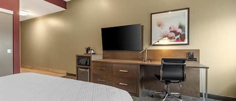 A hotel room with a bed, a desk with a chair, a flat-screen TV, a microwave, and a framed picture on the wall.