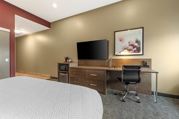 Quarto de hotel com uma cama, uma escrivaninha com cadeira, televisão de tela plana, micro-ondas e um quadro na parede.