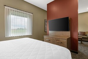 A hotel room with a bed, a TV mounted on the wall, a wooden dresser, and a window with a view. - Best Western Plus Dauphin (Dauphin)