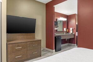 A hotel room with a wooden cabinet, a flat-screen TV, a sink with a mirror, and a compact refrigerator. - Best Western Plus Dauphin (Dauphin)