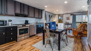 A modern kitchen with dark cabinets, stainless steel appliances, and a dining area with a wooden table and chairs.